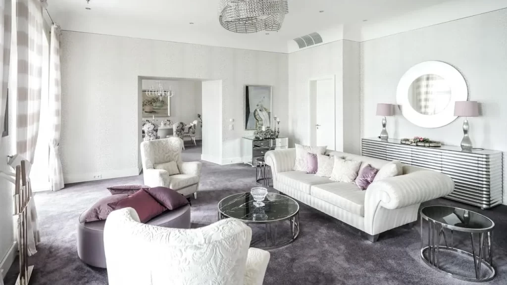 Experimenta el lujo en una habitación exclusiva en el hotel Austria Falkensteiner Schloss, equipada con una elegante sala y comedor. El diseño interior, que combina tonos blancos con toques morado, crea un ambiente sofisticado y acogedor.