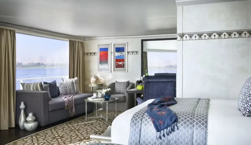 habitación ubicada en el barco santuario, con una cama amplia, un mini comedor y un sillón donde se puede ver por el ventanal el mar