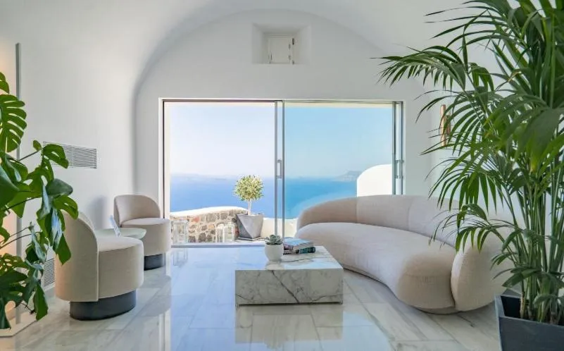 habitación con sillones blancos y una puerta de vidrio corrediza con salida al balcón con vista al mar.
