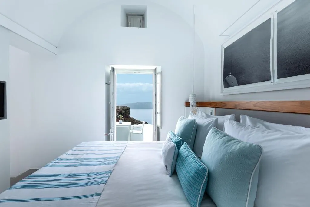 habitación con cama amplia y una puerta al frente para salir al balcón y disfrutar de la vista al mar y de las montañas rocosas.