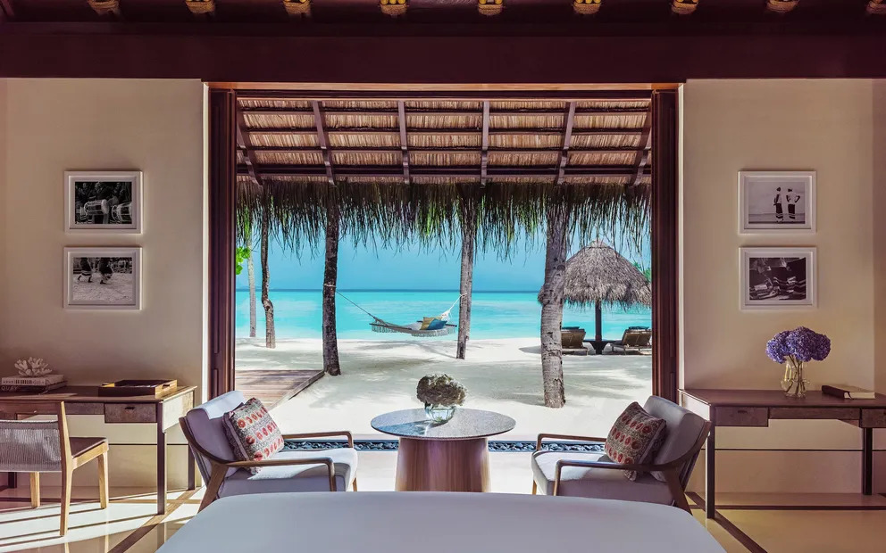 habitación con cama para dos personas, asientos cómodos con mesa y una puerta que conecta a la playa donde se puede ver el mar y relajarse en la amaca