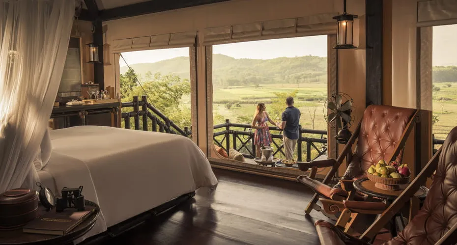 pareja disfrutando de una vista desde el balcón de su habitación con una cama para dos personas y dos sillas cómodas de madera