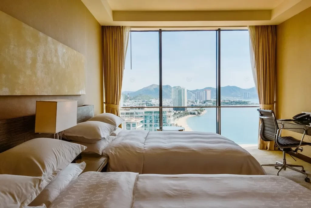 habitación con dos camas dobles, un escritorio y un ventanal grande con vista al mar.