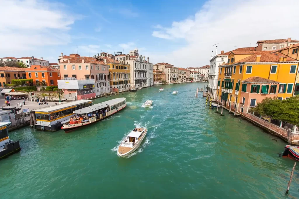 Explora la encantadora ciudad de Venecia, donde los edificios se reflejan en las aguas de sus canales y los yates navegan, creando un paisaje único.