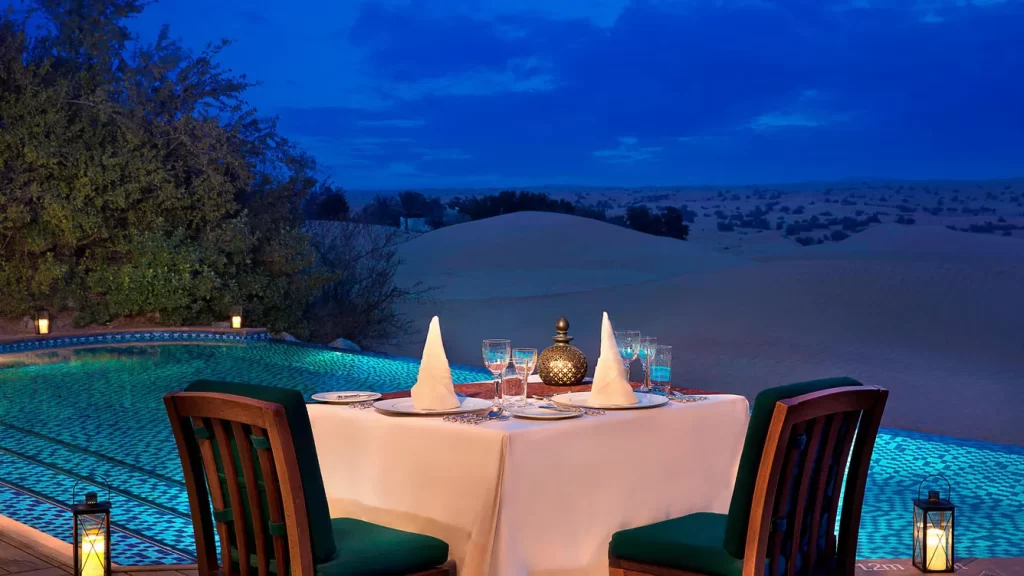 cena romántica para dos personas al lado de la piscina disfrutando de la vista del desierto en el anochecer.