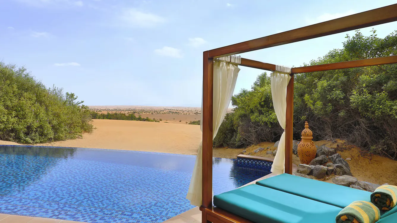 piscina con sillas cómodas de descanso, rodeada de zona verde y con vista al desierto