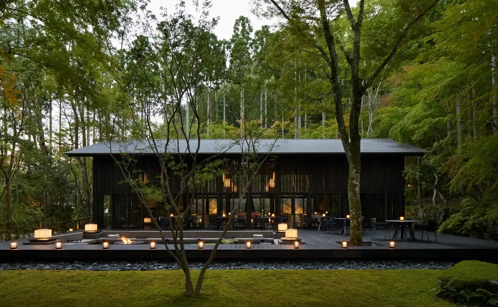 restaurante lujoso con mesas adentro y al aire libre rodeada de lamparas para iluminar el lugar, rodeada de arboles y zona verde en la mañana.