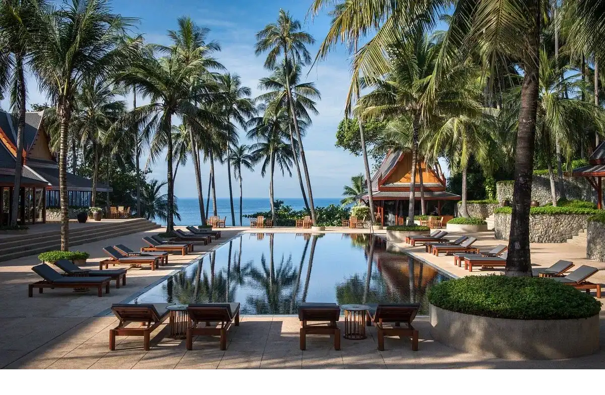 piscina de agua natural con sillas de descanso, rodeada de jardines y palmeras con vista al mar