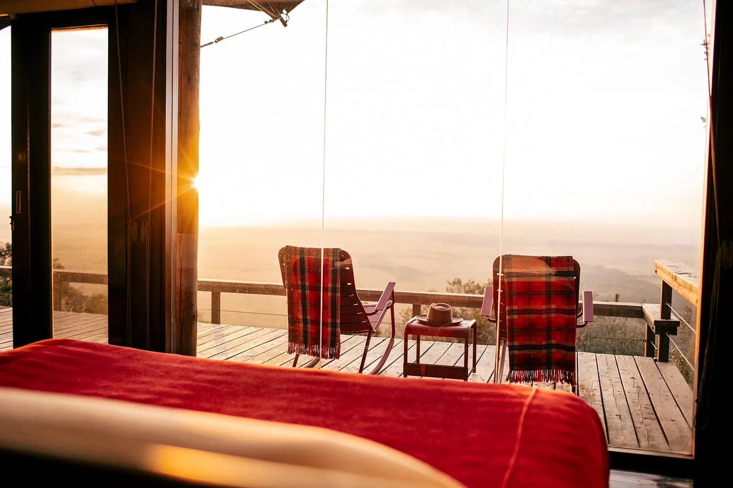 habitación amplia con una cama y un ventanal grande que conecta al balcón con sillas y mesa y una vista a la sabana