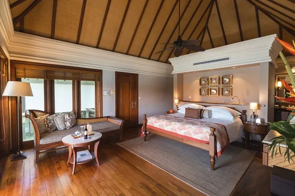habitación de lujo con una cama para dos personas, dos nocheros cada uno con una lampara para una mejor iluminación, un sillón amplio y una mesa.