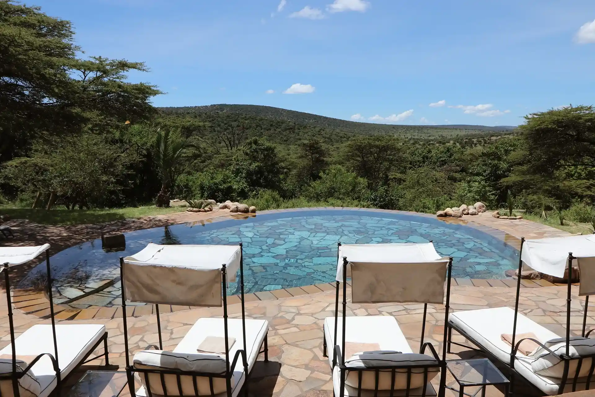 piscina con sillas para acostarse y con vista a las montañas rodeada de arboles y plantas