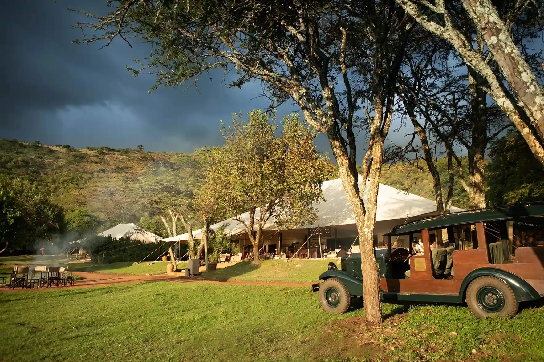 Camps grandes con salida a la zona verde con mesa y sillas y un jeep para recorrer el safari