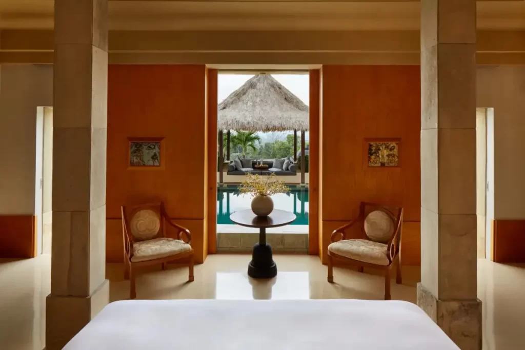una habitación con cama doble, sillas de madera, una mesa decorativa y una piscina de agua clara