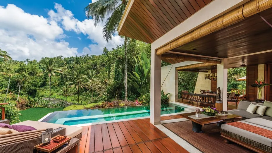 sala con asientos cómodos una lujosa piscina con vista a los arboles y palmeras