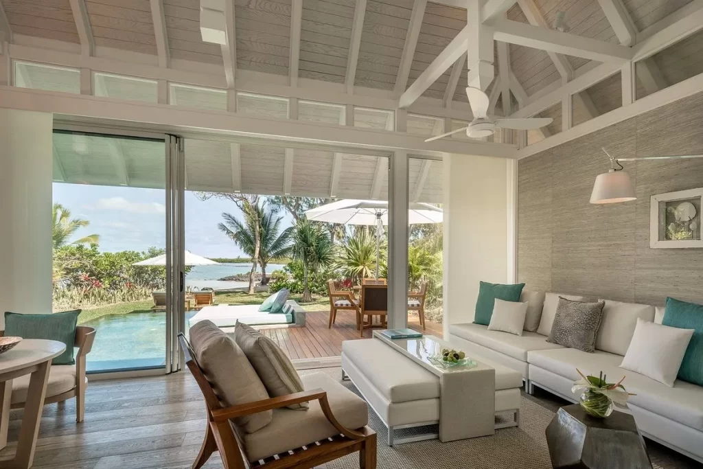 sala estar con sillones cómodos de color blanco, una mesa con silla y en las afuera una piscina con vista al mar
