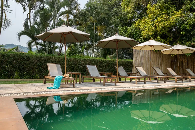 piscina de agua natural y al rededor sillas de madera con sombrilla
