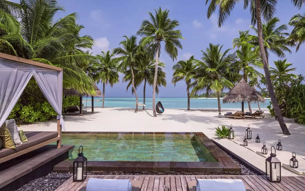piscina de lujo junto a la playa rodeada de palmares y sillas de descanso para relajarte en un ambiente agradable.