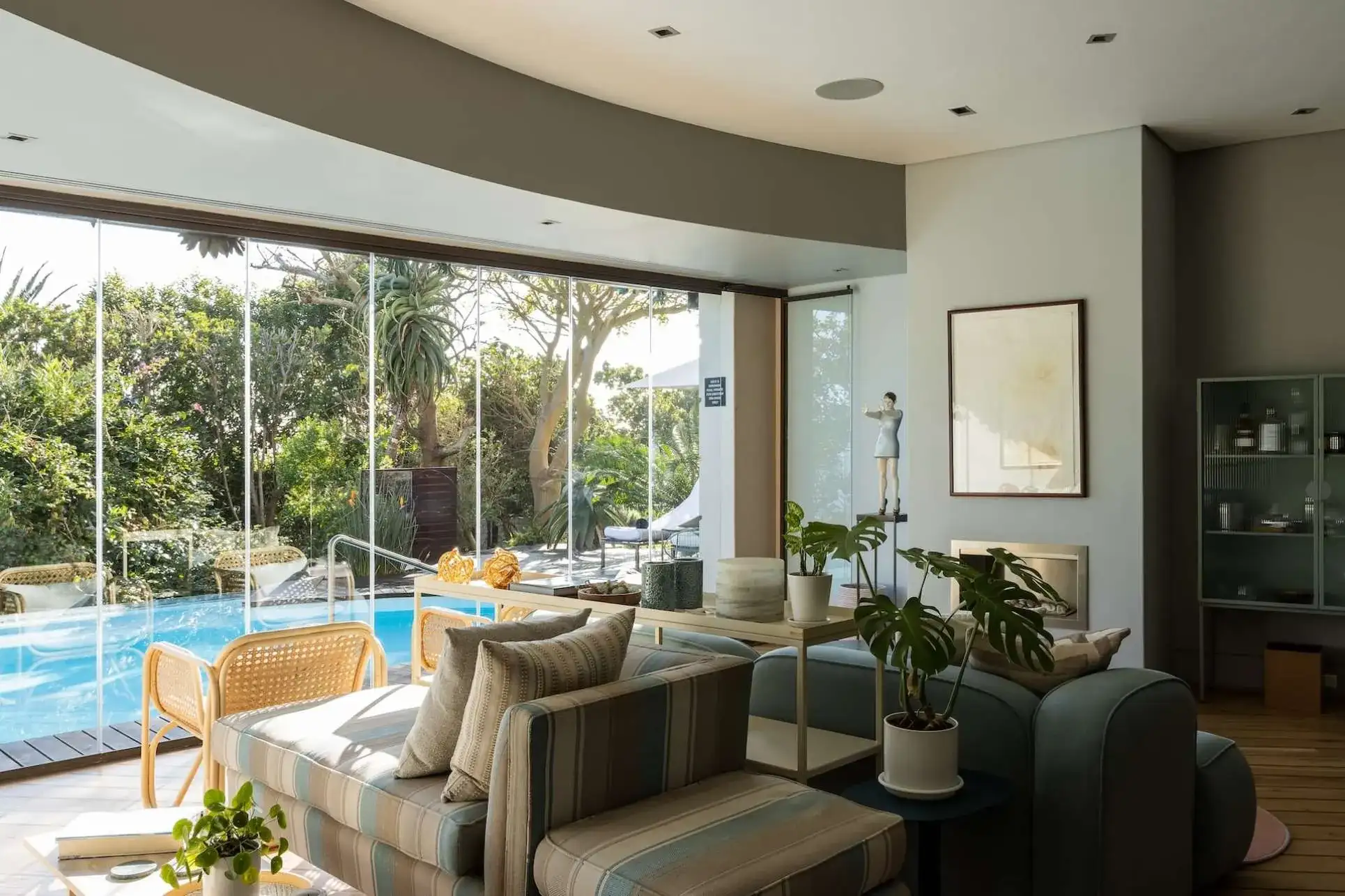 casa amplia con una decoración moderna con plantas y sillones cómodos con un ventanal grande donde se puede ver la piscina