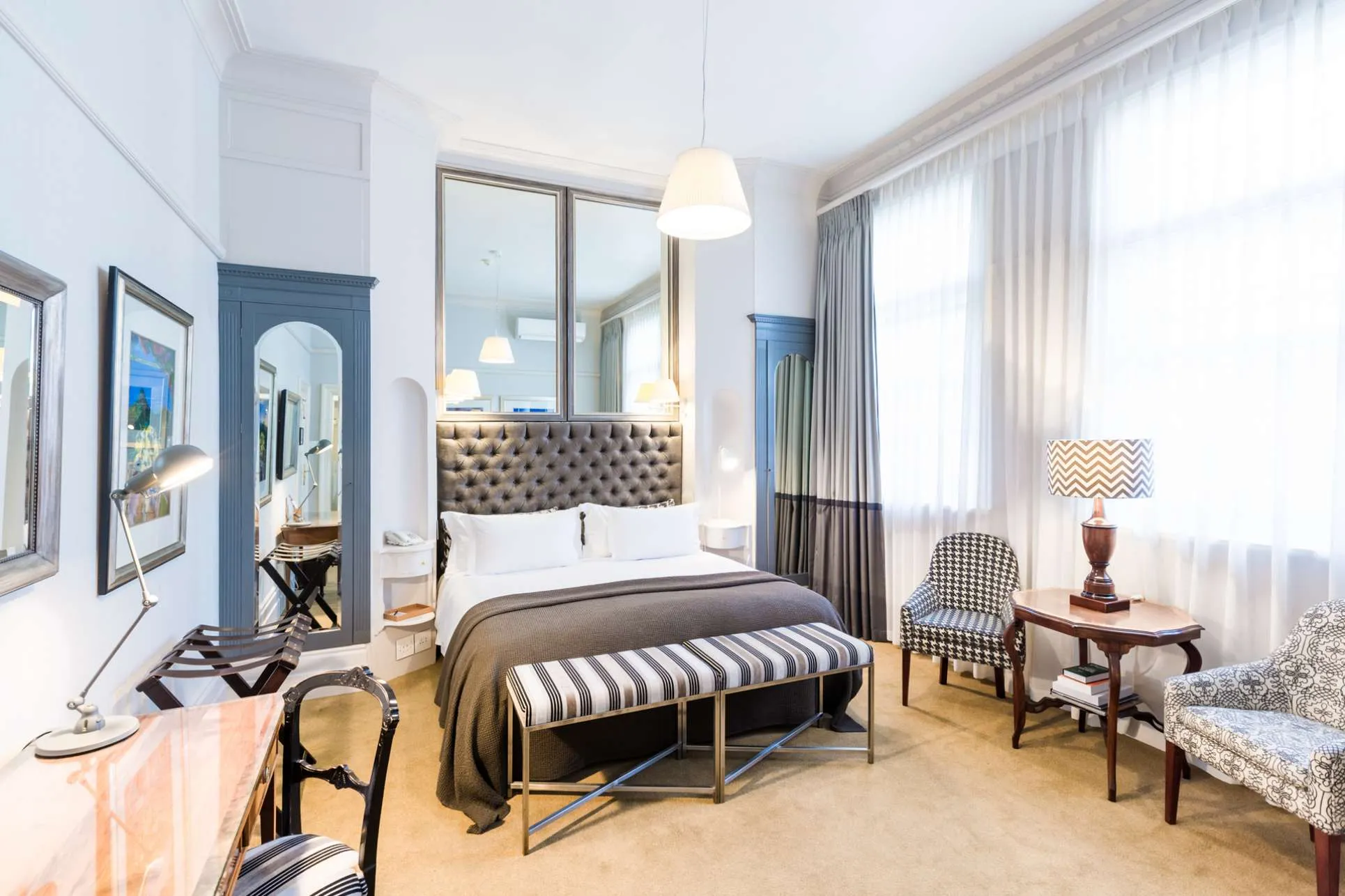 habitación con un diseño moderno, cama para dos personas, sillas y un escritorio con lampara.