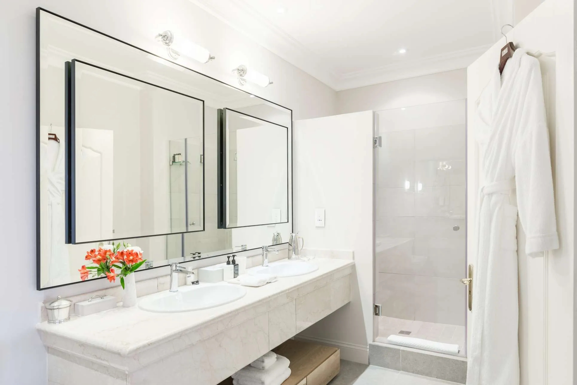 baño de lujo, con puerta en la ducha de de vidrio transparente, espacio amplio y iluminación, con dos elegantes fregaderos.