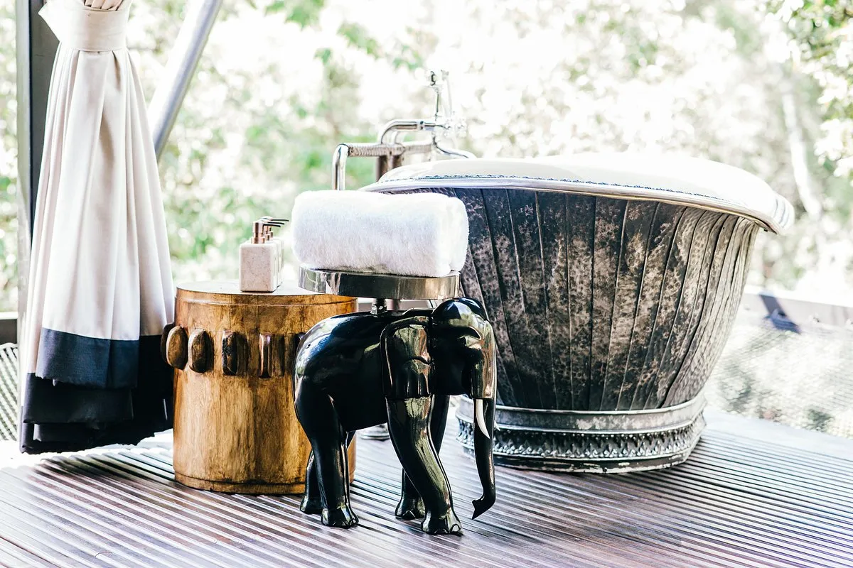 elegante baño con una mesa de madera practico para poner los implementos de aseo personal, junto a una figura decorativa de elefante con soporte para las toallas de baño, creando un ambiente sofisticado.