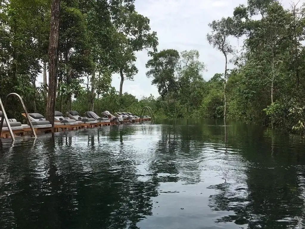 piscina de agua natural en Shinta Mani salvaje, rodeada de árboles y un entorno natural para disfrutar de la relajación. Con cómodas sillas de descanso a su alrededor.