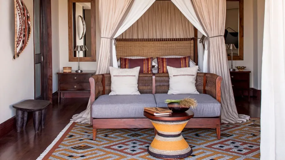habitación con cama para dos personas, sillón de madera con cojines de color café y mesa decorativa