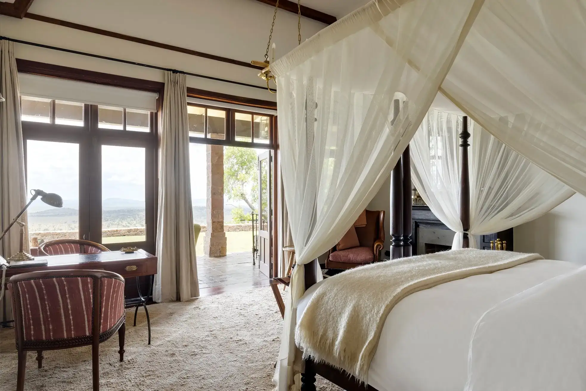 habitación amplia con cama para dos personas un escritorio con lampara y dos asientos con una salida para disfrutar de la vista