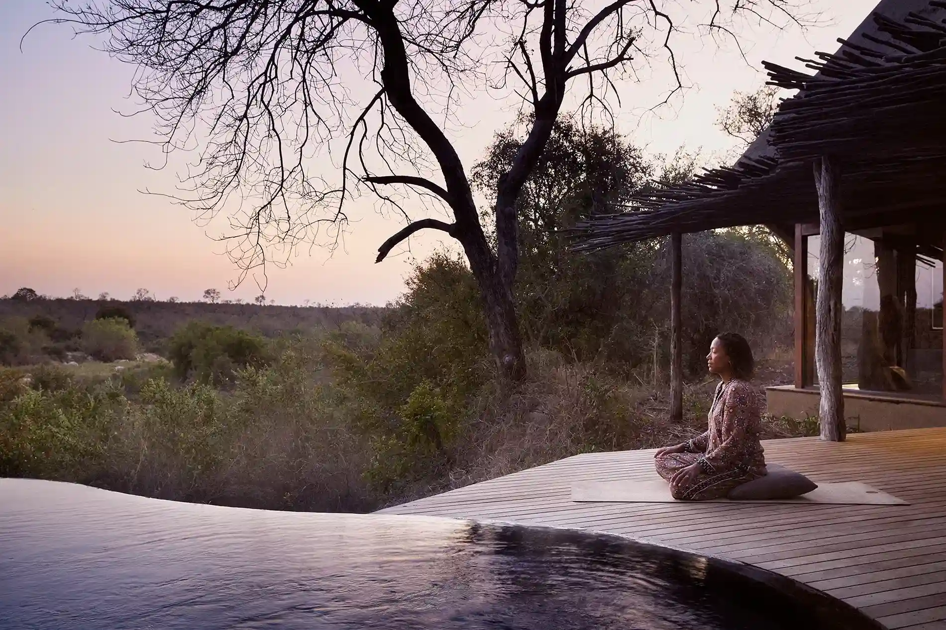 mujer realizando meditación a lado de la piscina y disfrutando de una hermosa vista