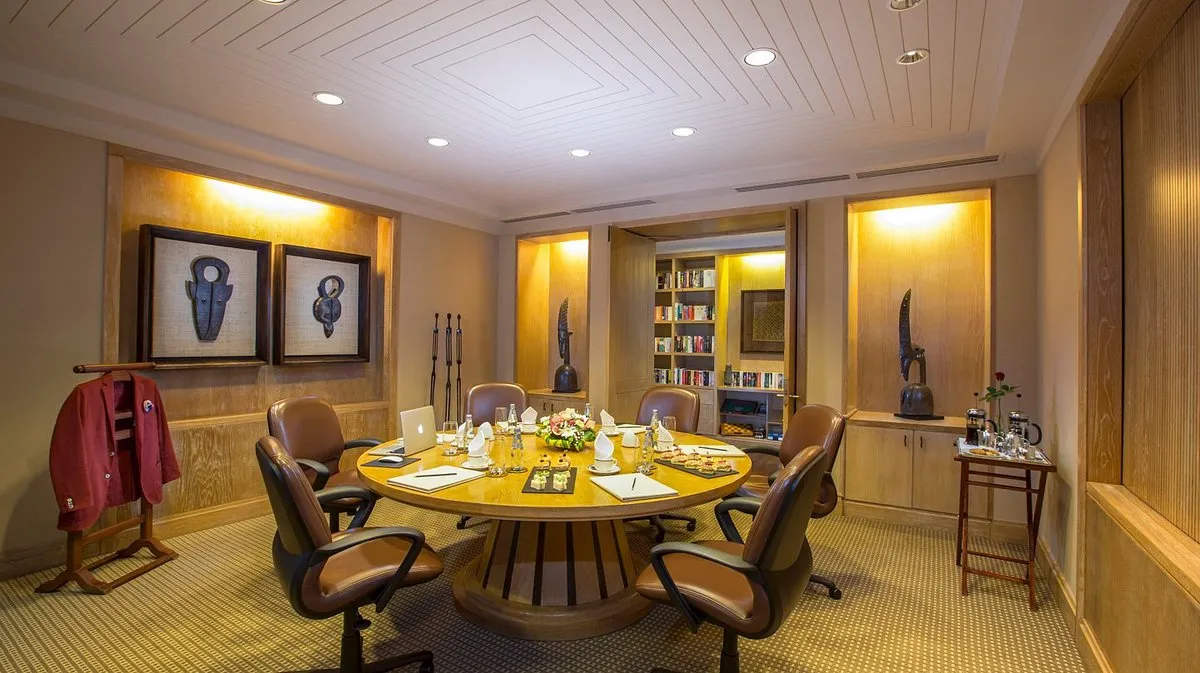 despacho con mesa, asientos ejecutivos, una decoración moderna, biblioteca, esculturas y una mesa con comida