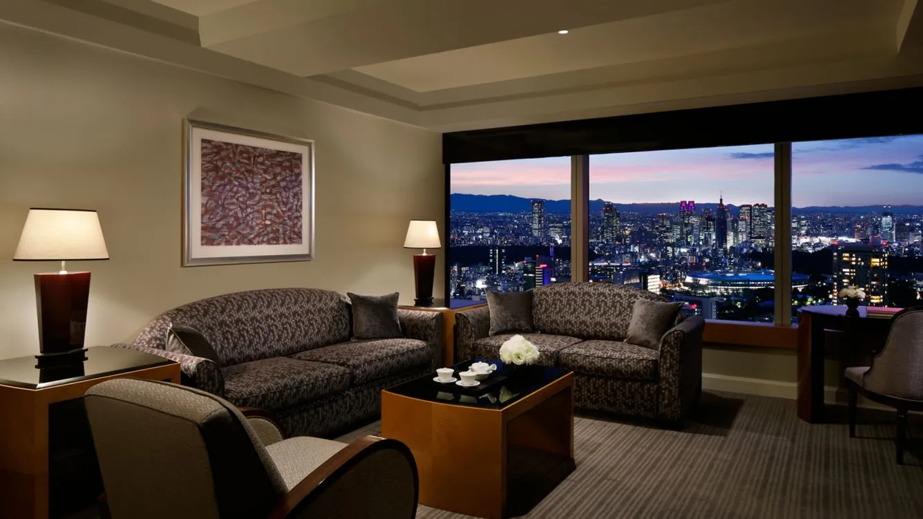 lujosa habitación con sala, cuenta con sillones cómodos, mesa de noche, buena iluminación y un ventanal con vista a la ciudad.
