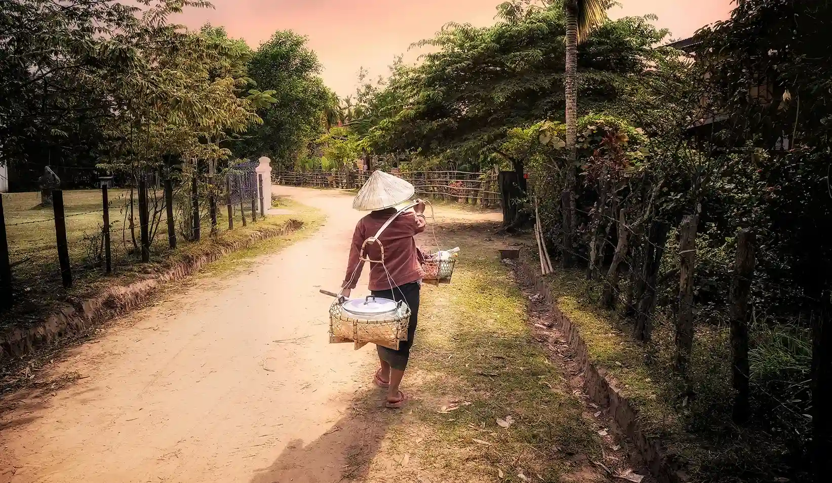 señora cargando unas ollas y caminando por una carretera rodeada de zona verde