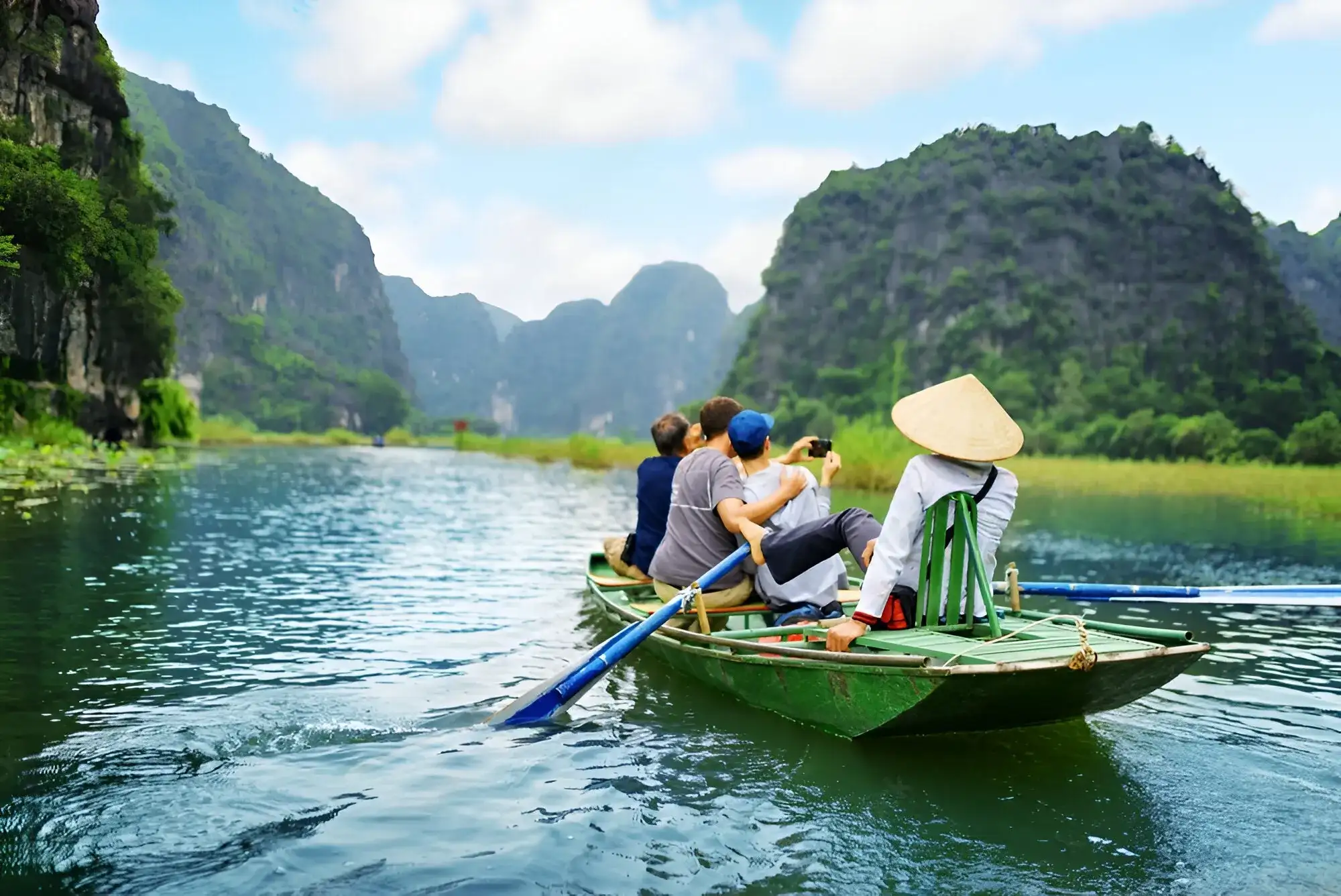 turista recorriendo el rio de Vietnam en canoa y tomando fotos a las grandes montañas