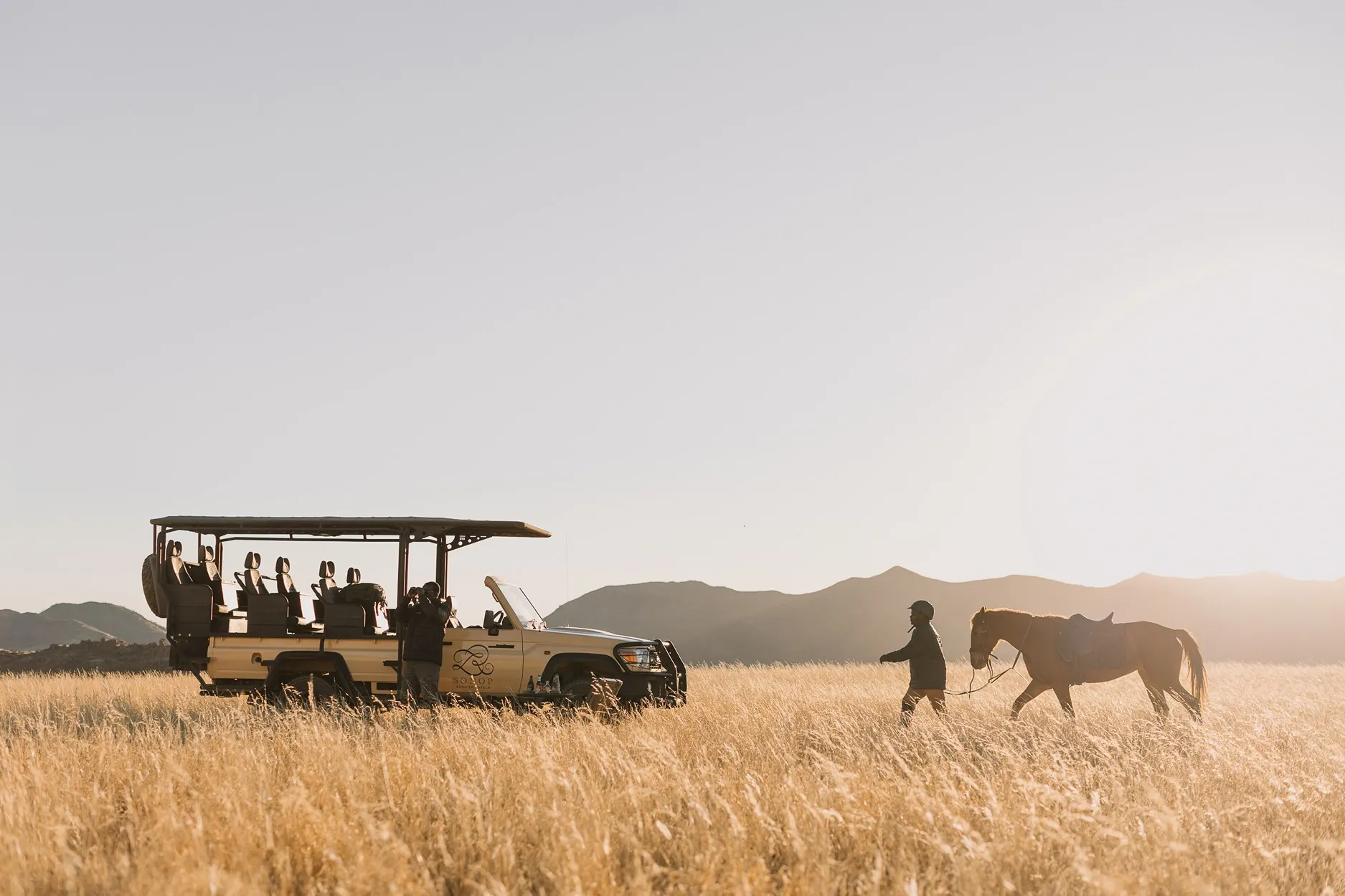 jeep de color beige, con varios asientos de color negros ,dos guías que están viendo el desierto en el safari