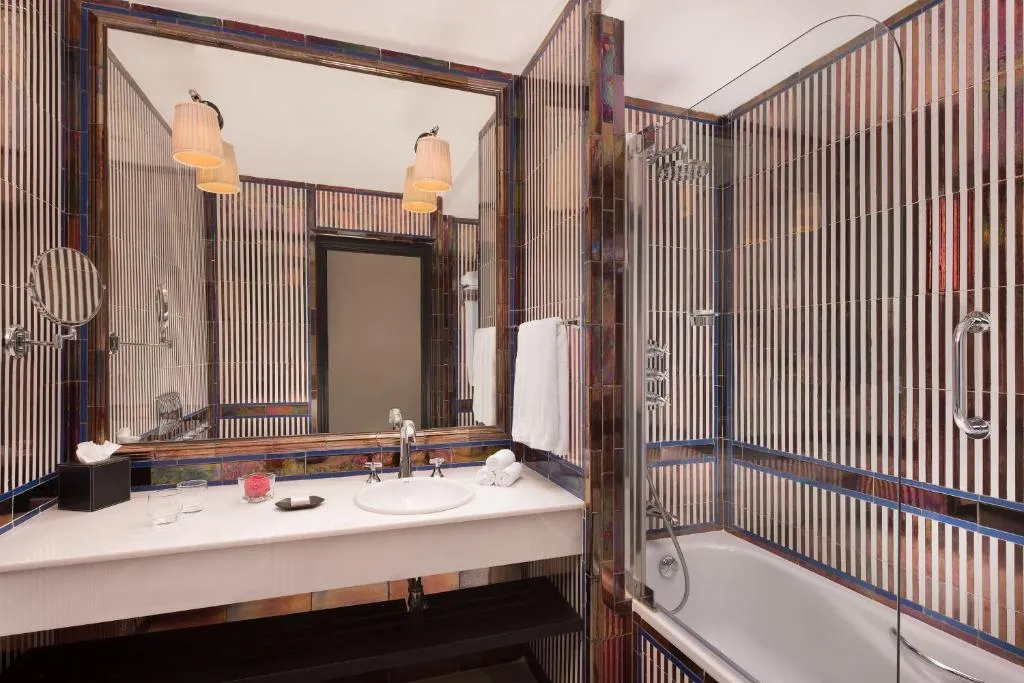 Baño en el Hotel Alfonso XIII, con una elegante tina, un gran espejo que amplía el espacio y un lavamanos equipado con todos los implementos de aseo personal. Un lugar perfecto para relajarte y disfrutar de comodidades de lujo.