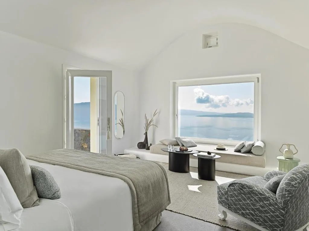 suite con cama amplia, sillones, una ventana con vista al mar y una puerta donde vas a poder salir al balcón.