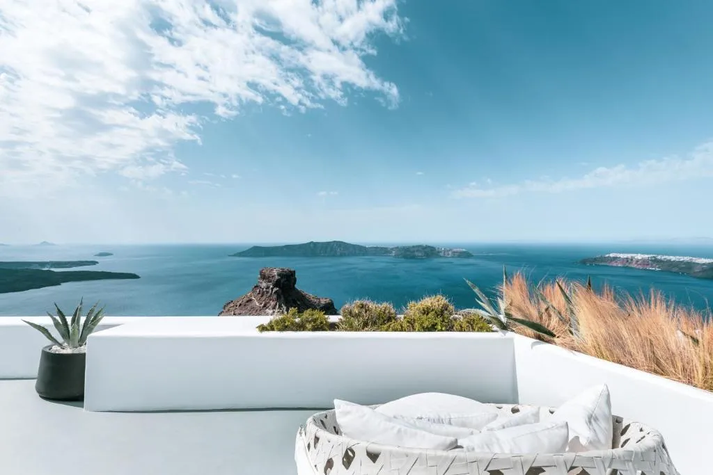 balcón con puf de color blanco cómodo rodeada de jardín con vista al mar en Santorini.