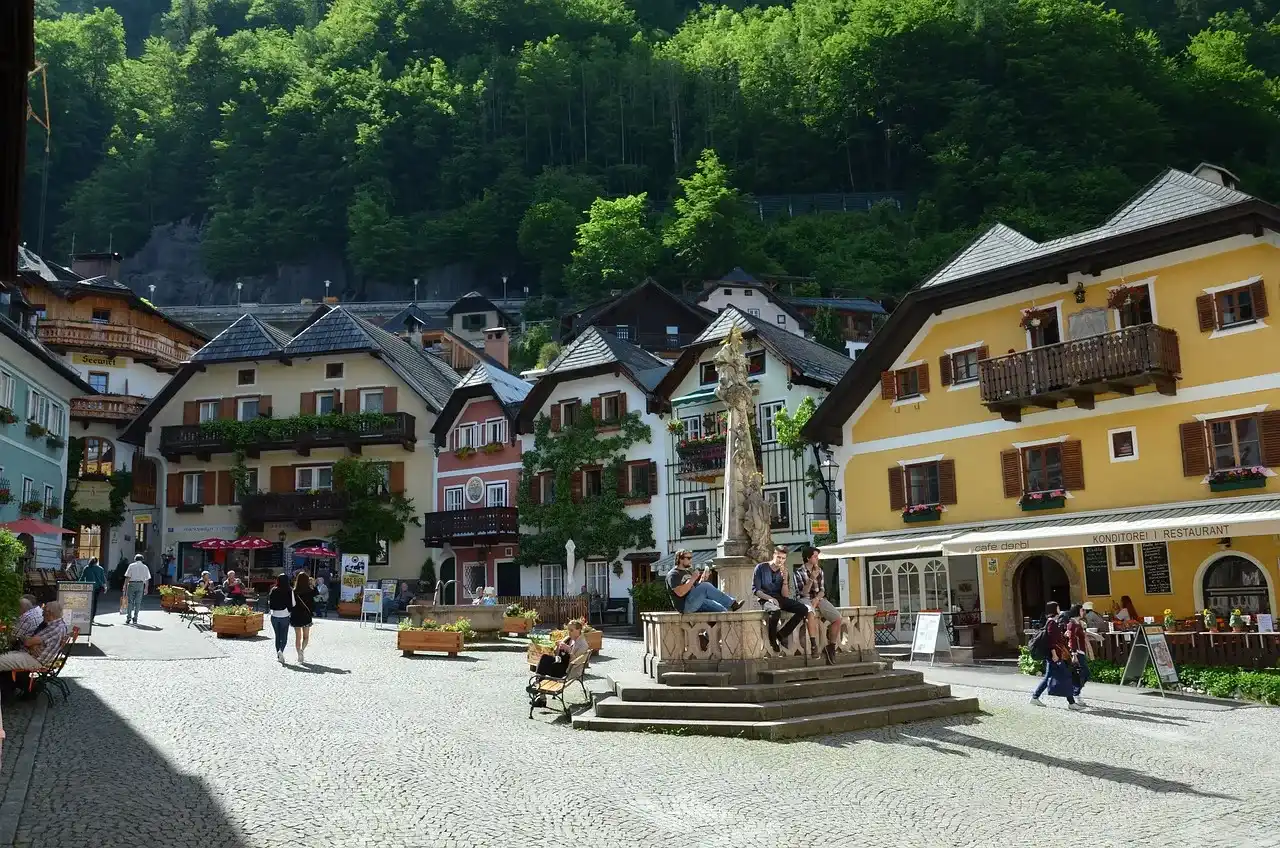 personas paseando por las calles de Austria, rodeadas de casas típicas y árboles, un paisaje perfecto para quienes disfrutan de caminar por barrios tranquilos.