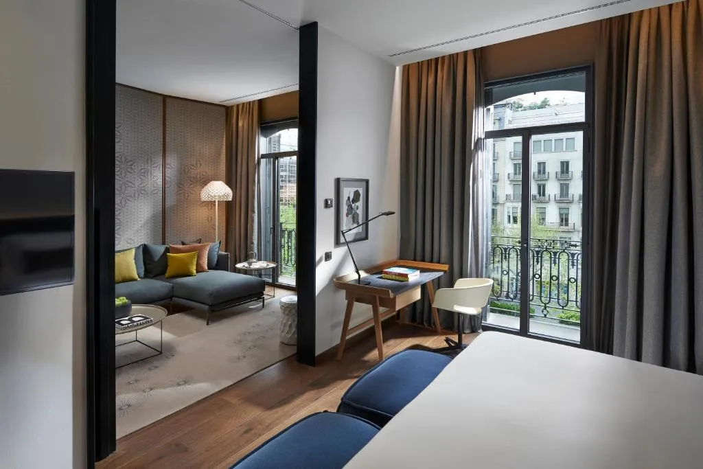 Habitación espaciosa con cama doble, una sala acogedora y un gran ventanal con vista a la ciudad.