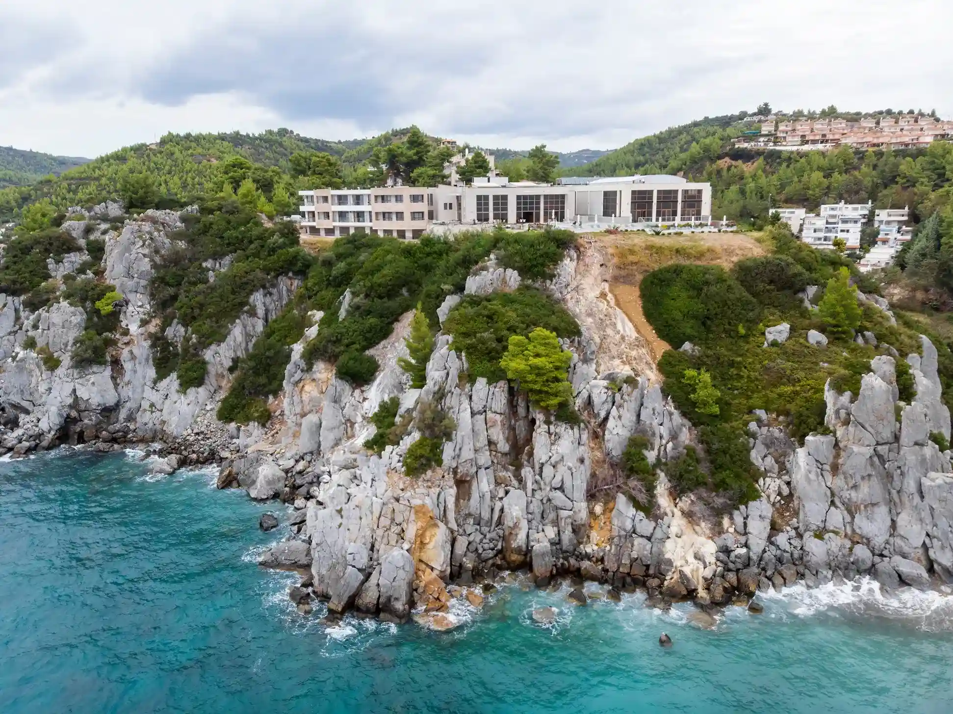 edificios en montañas rocosas rodeado de zona verde junto al mar cristalino en Grecia