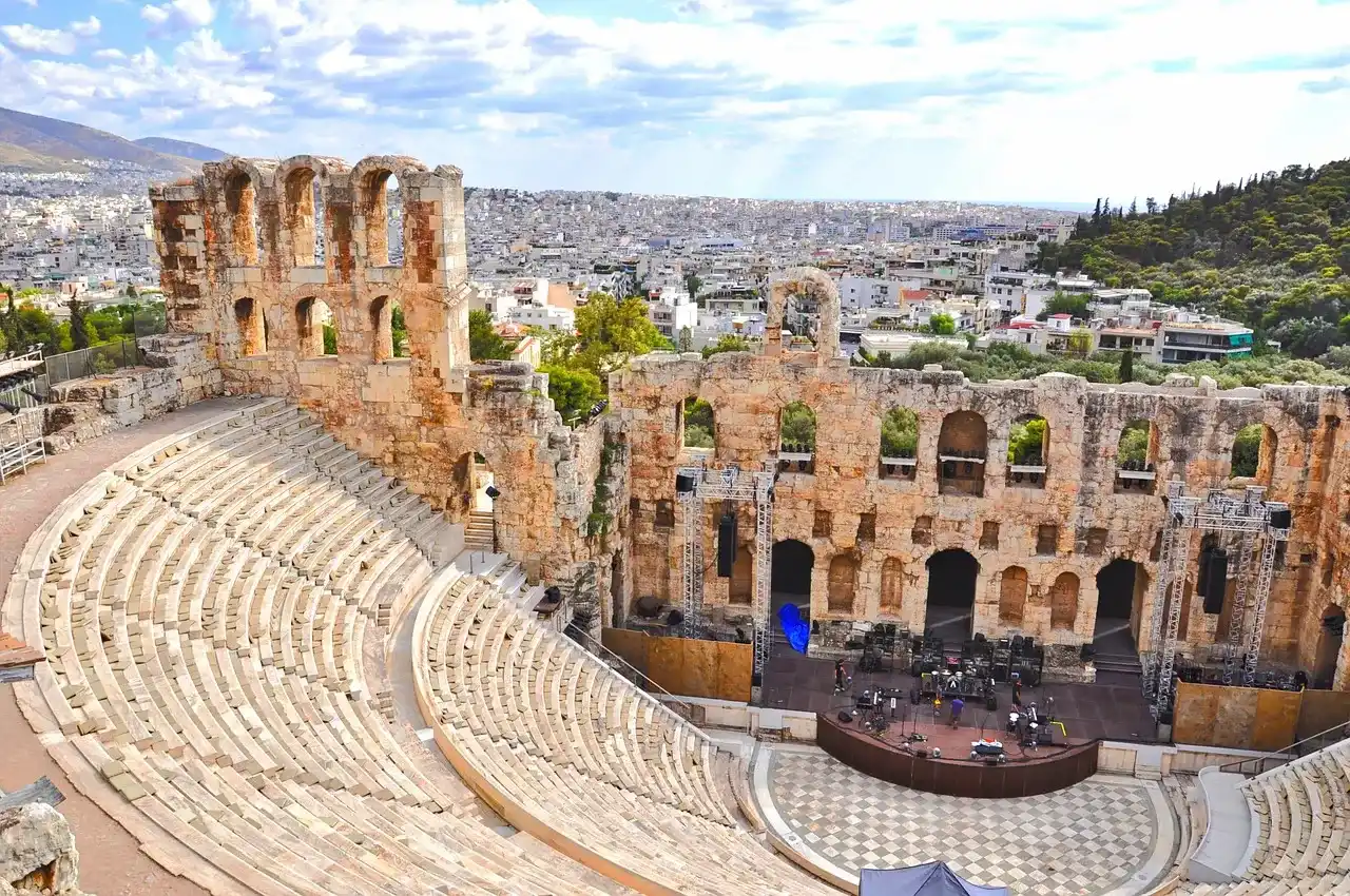 estadio de estructuras rocosas rodeado de mas edificios y zona verde, donde vas a poder ir a conciertos o escuchar música típica en Grecia.