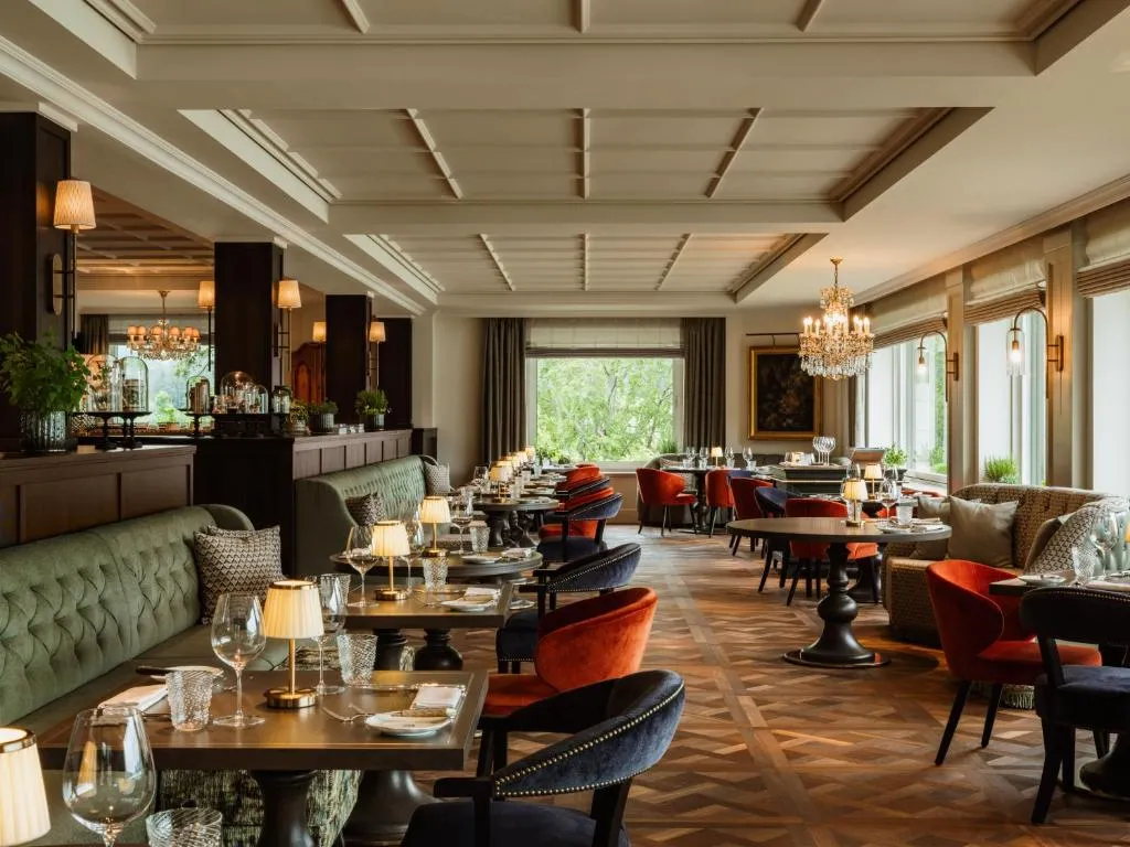 Disfruta de una comida en el lujoso restaurante Rosewood Schloss Fuschl, donde podrás relajarte junto a un ventanal con vistas espectaculares a la zona verde.