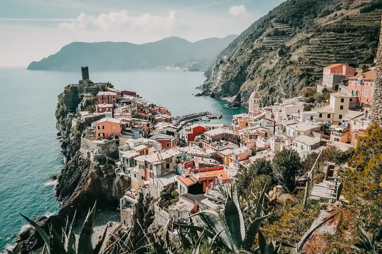 edificios ubicados en las montañas rocosas, rodeado de arboles con vista al mar.