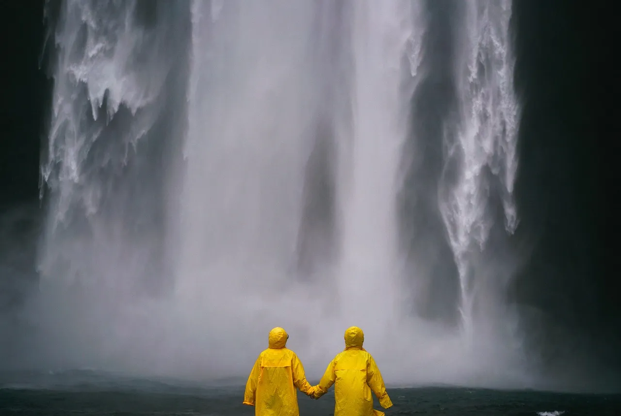 pareja agarrándose de las mano, disfrutando del agua cayendo de la cascada.