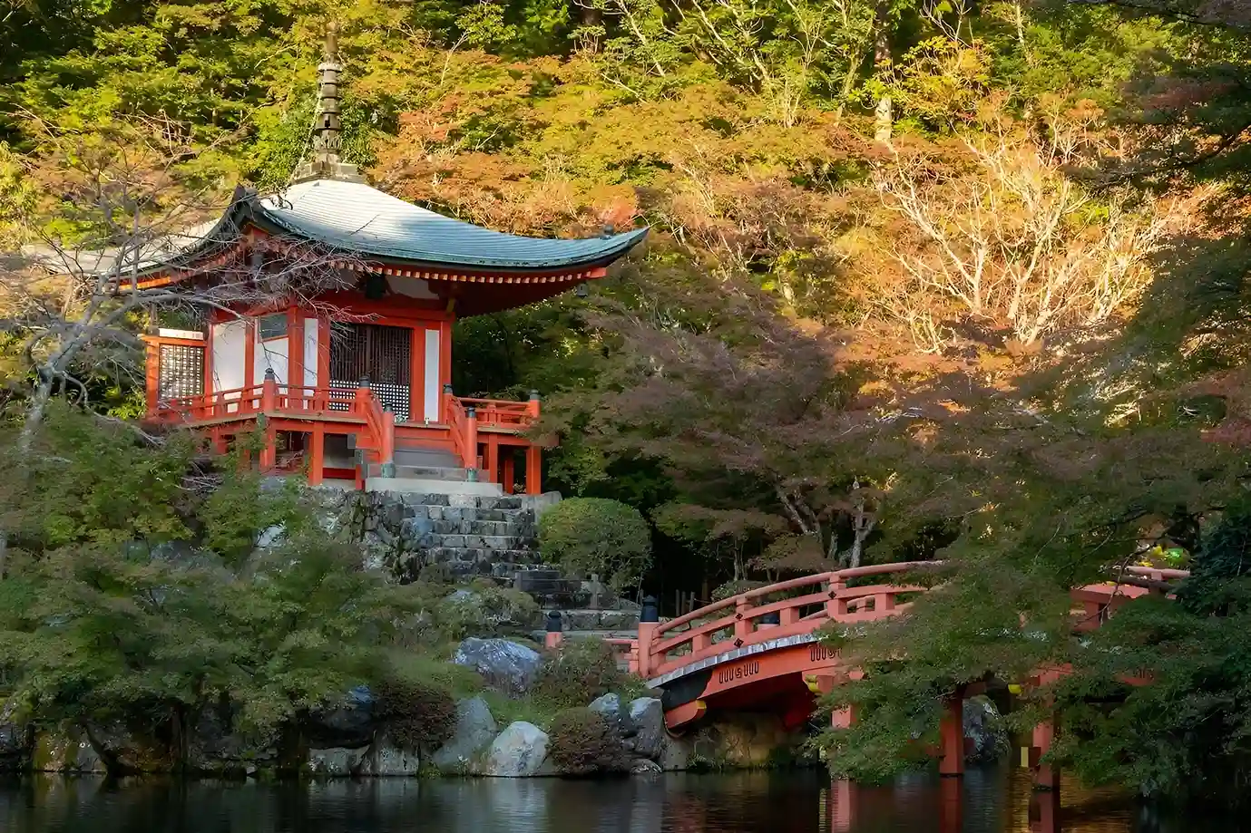 templo rojo ancestral rodeado de arboles, bajo un puente donde corre un lago.