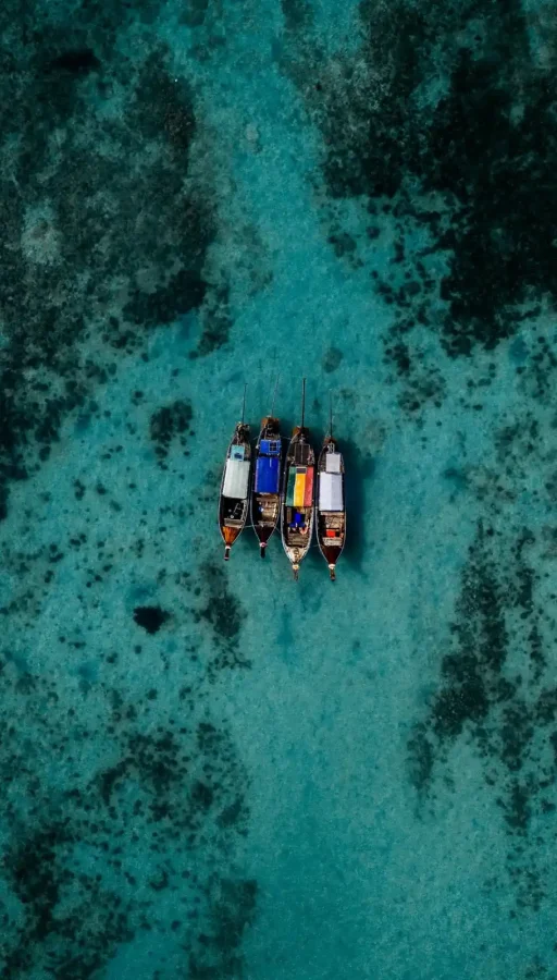 journale te ofrece vistas panorámica en las Islas Phi Phi, Tailandia, con el mar turquesa y cuatro barcos tradicionales tailandeses flotando en aguas cristalinas.